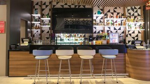 Zona de bar con diseño moderno, que incluye un televisor de pantalla plana, taburetes y estantes llenos de botellas.