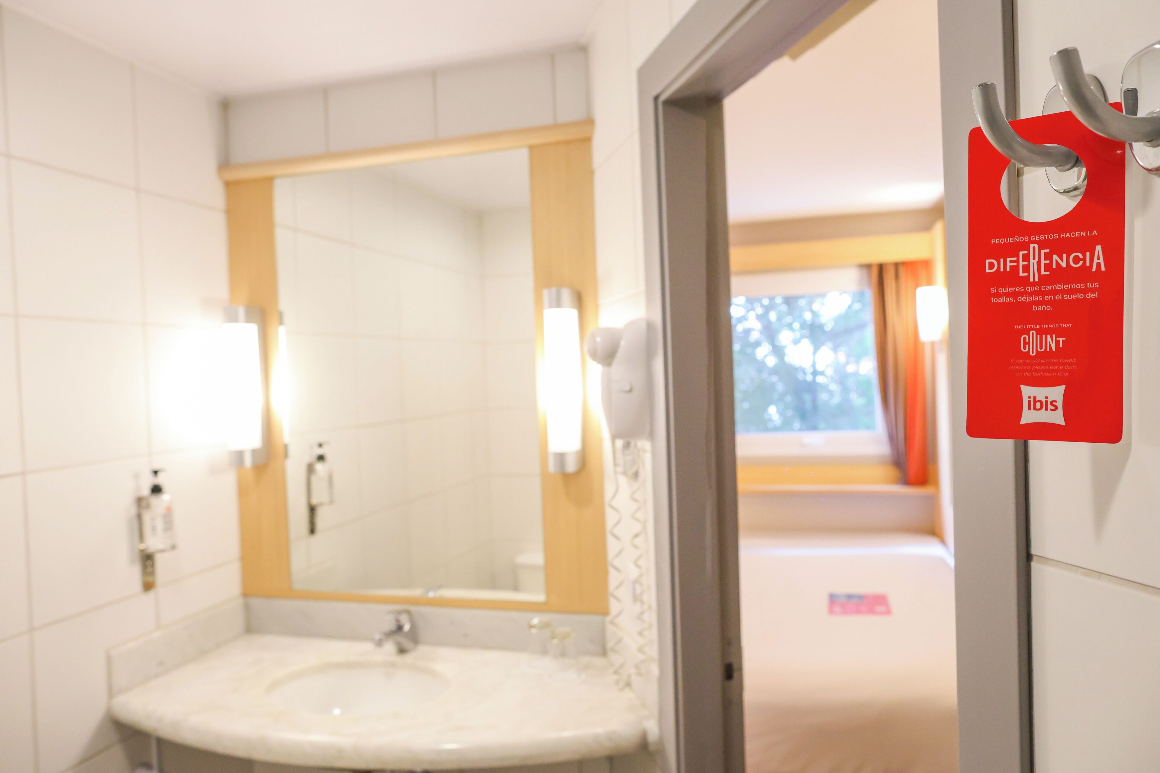 A hotel bathroom with a sink, mirror, and a sign on the wall.