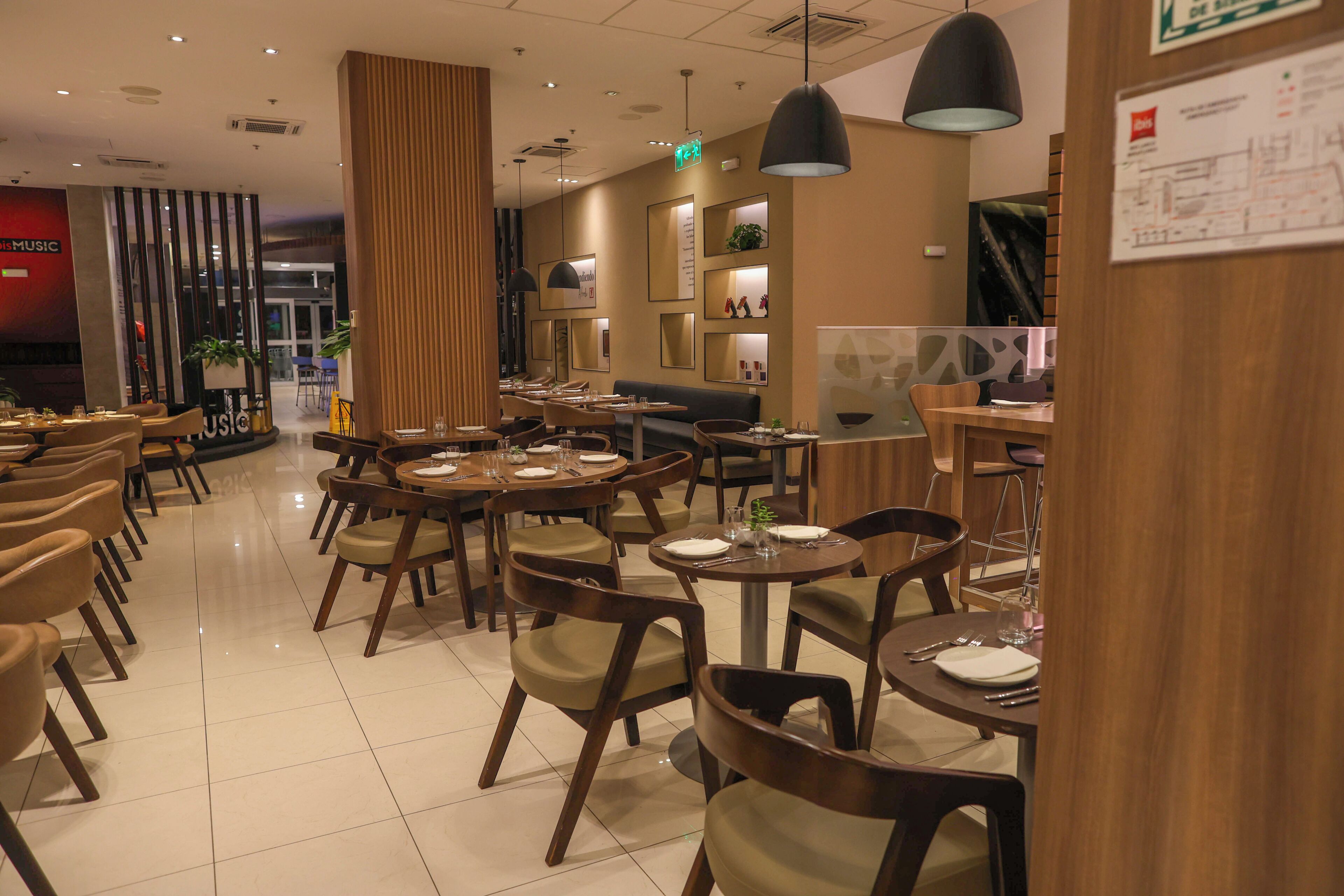 Un restaurant doté de nombreuses tables et chaises, d’un plafond haut avec des luminaires suspendus et d’un décor intérieur moderne.