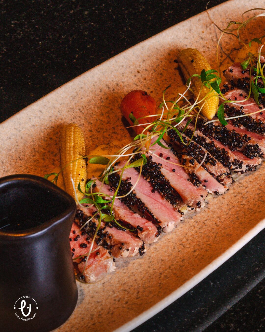 A plate of sliced meat with black caviar, corn, and a small bowl of sauce.