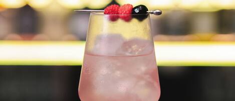 A cocktail with a raspberry garnish in a tall glass on a bar counter.