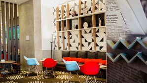 Un área de descanso moderna con un sofá, sillas coloridas, un tapete estampado y una pared decorativa con estanterías.