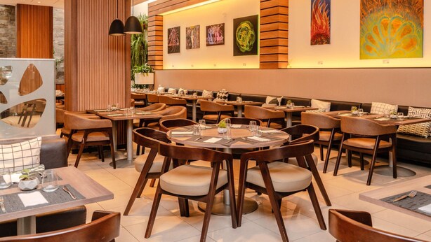 Un interior de restaurante moderno con mesas redondas, sillas acolchadas y una barra larga.
