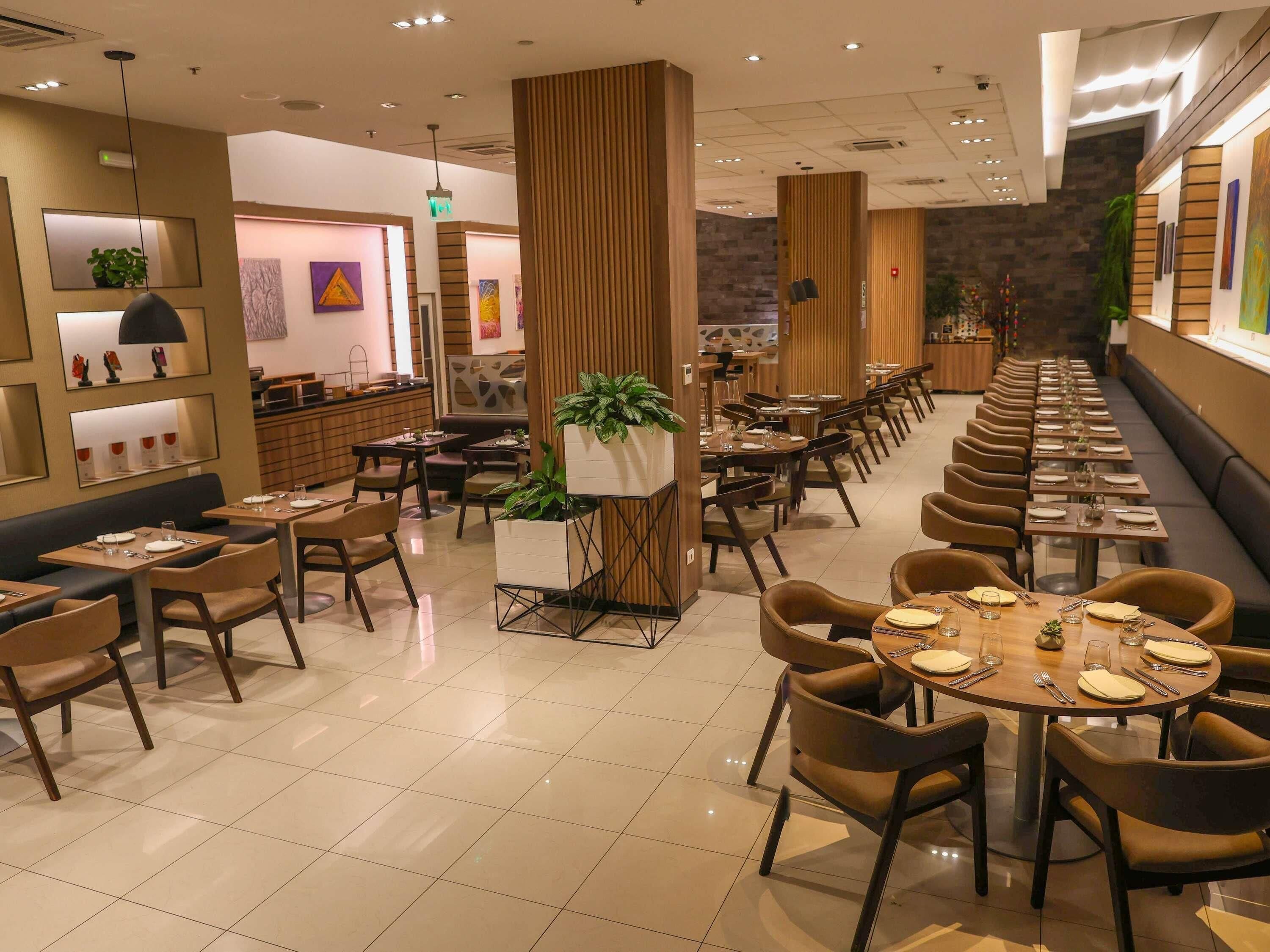 A modern restaurant with multiple dining areas, including booths and tables, and a bar area.