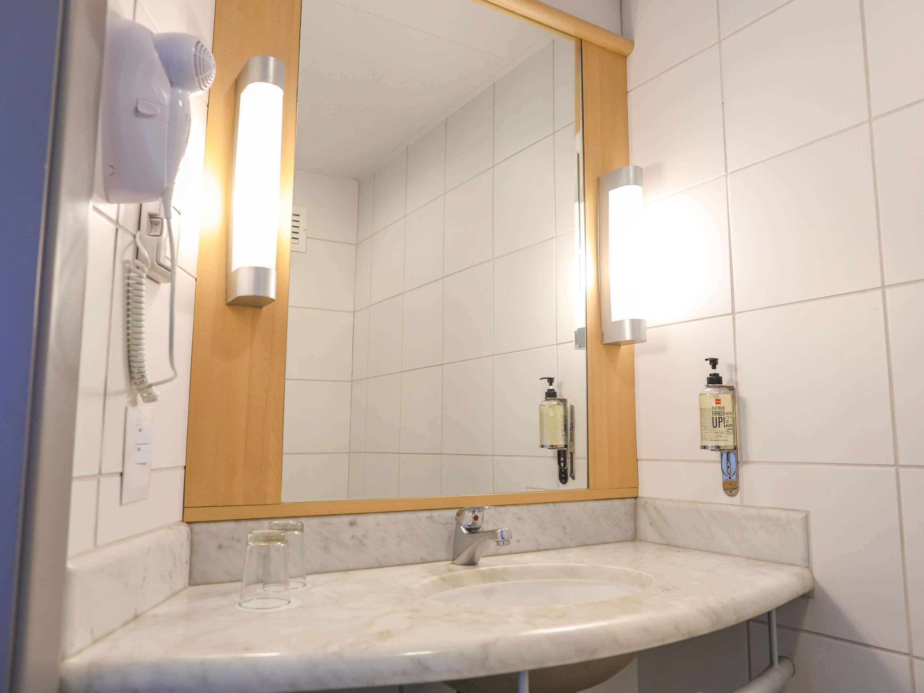 Ein Badezimmer mit weißem Waschbecken, einem Spiegel mit Holzrahmen und zwei Wandleuchten.