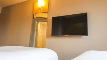 Habitación de hotel con dos camas, un televisor de pantalla plana montado en la pared y una lámpara en el techo.