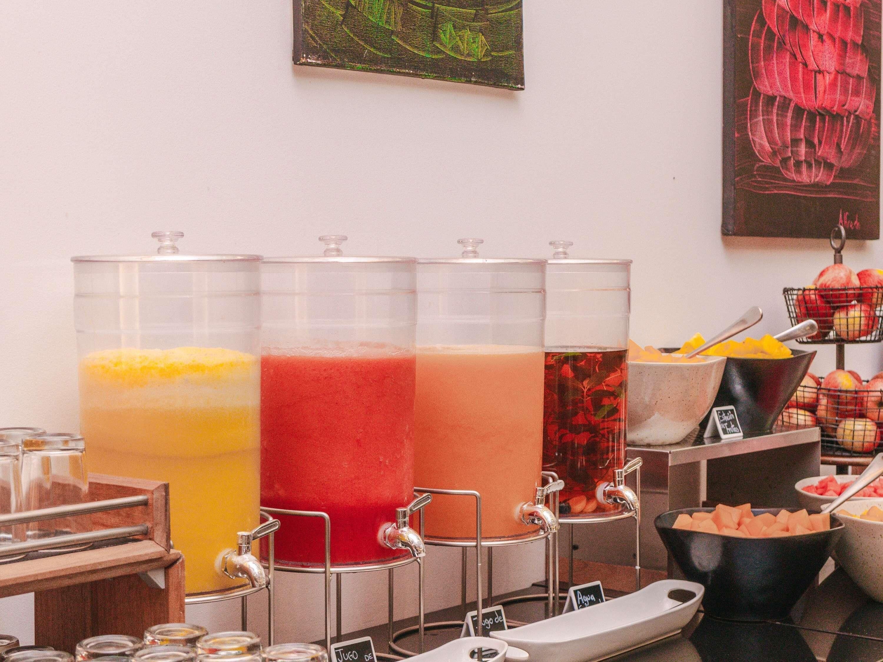 A juice bar with multiple dispensers and a variety of fruits and vegetables.