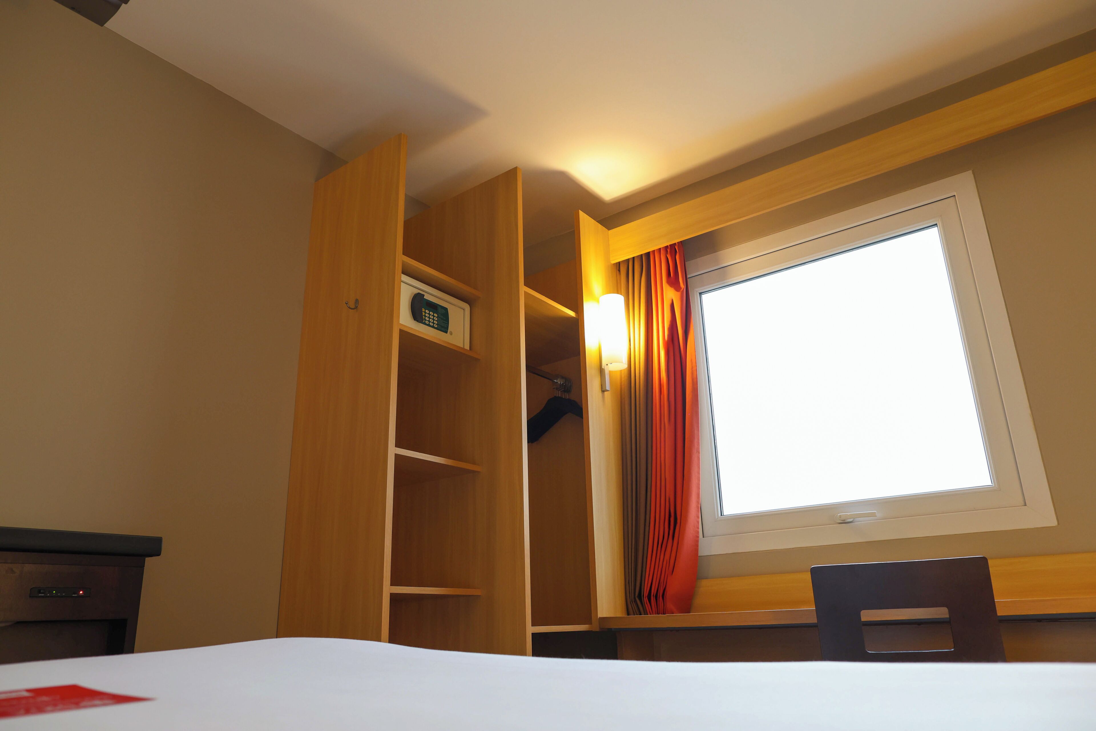 Une chambre d’hôtel avec un lit, une armoire en bois, un bureau et une fenêtre avec des rideaux.
