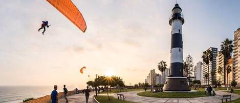 A coastal park with a lighthouse, a paved walkway, and a grassy area.