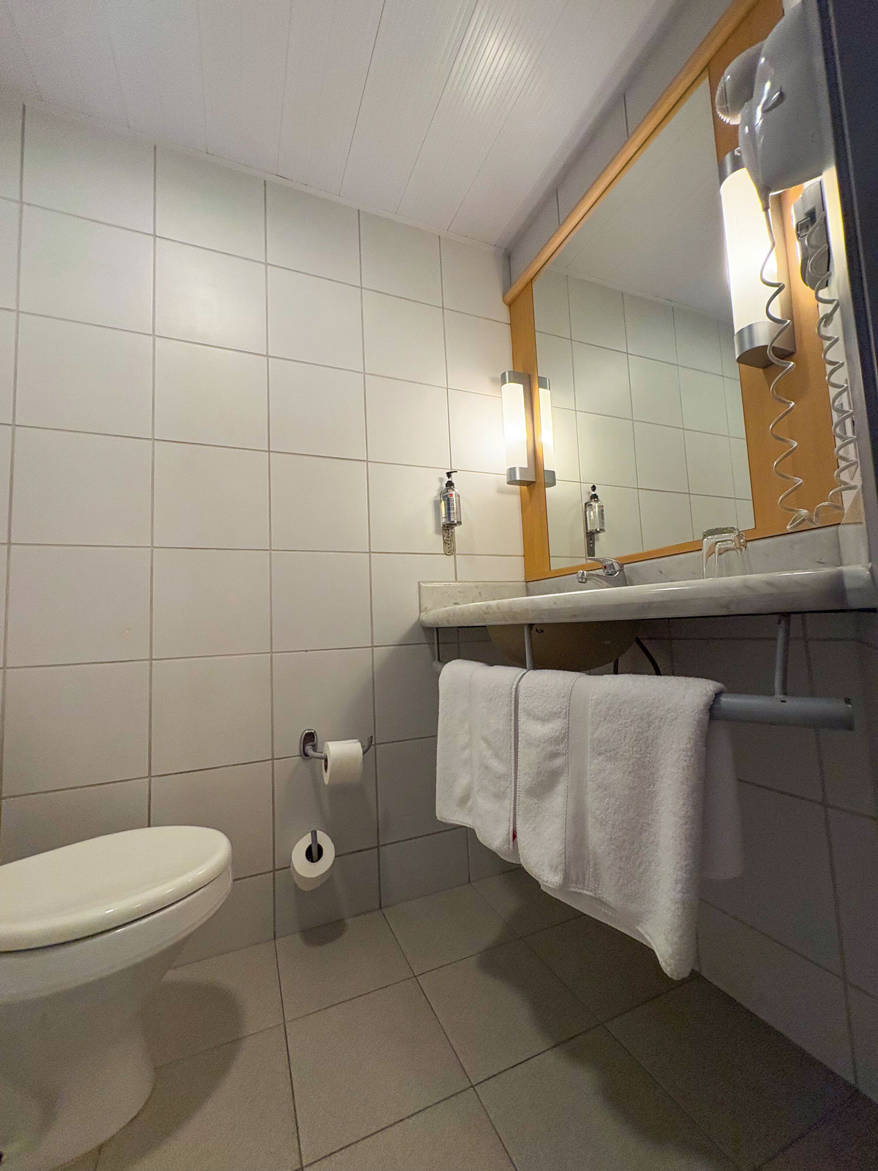 Un baño con inodoro, lavamanos con toalla y espejo.