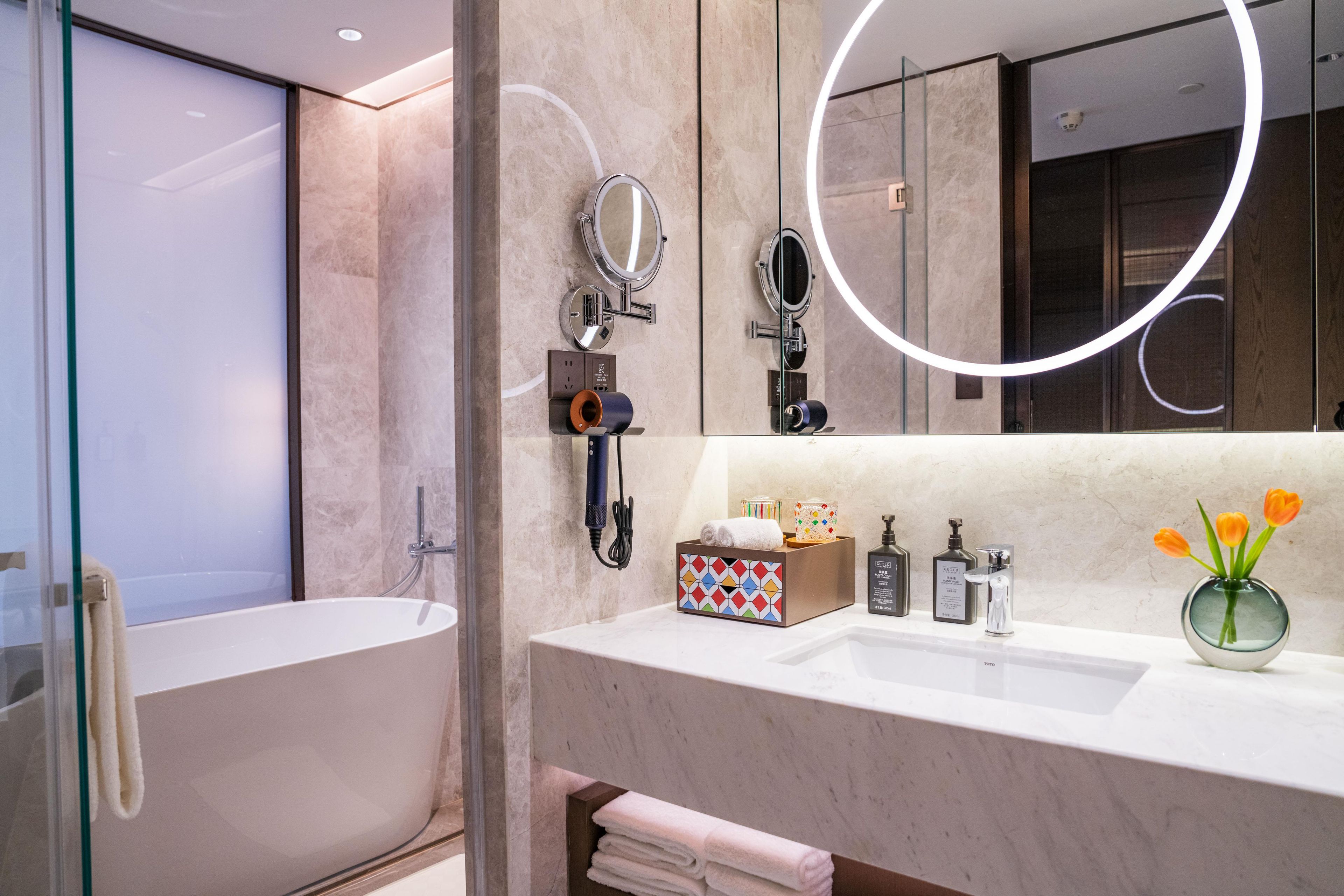 Un bagno moderno con una vasca da bagno indipendente, un mobile lavabo con specchio e un vaso con fiori.