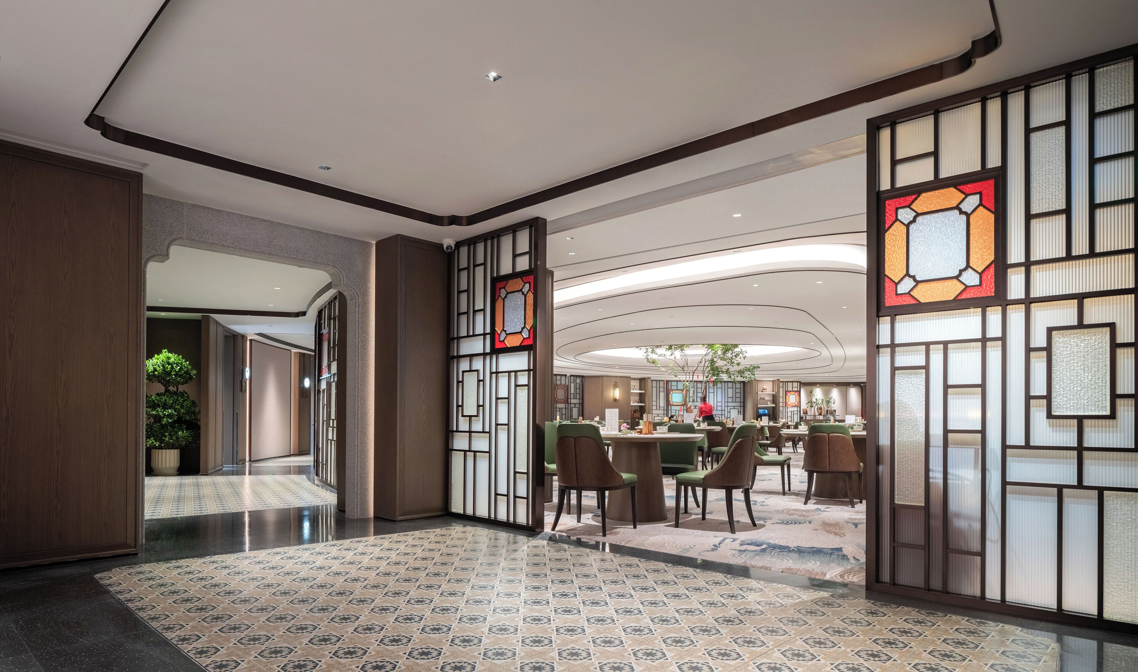 Un hall d’entrée spacieux au design moderne, avec un sol à motifs, un espace d’accueil et un coin salon équipé de chaises et de tables.