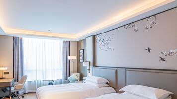 Habitación de hotel con dos camas, un escritorio, una silla, una lámpara y una pared decorada con un mural floral.