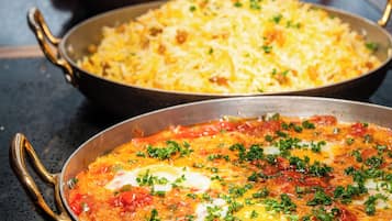 A variety of dishes in pans, including a pasta dish, a rice dish, and a tomato-based dish with herbs.