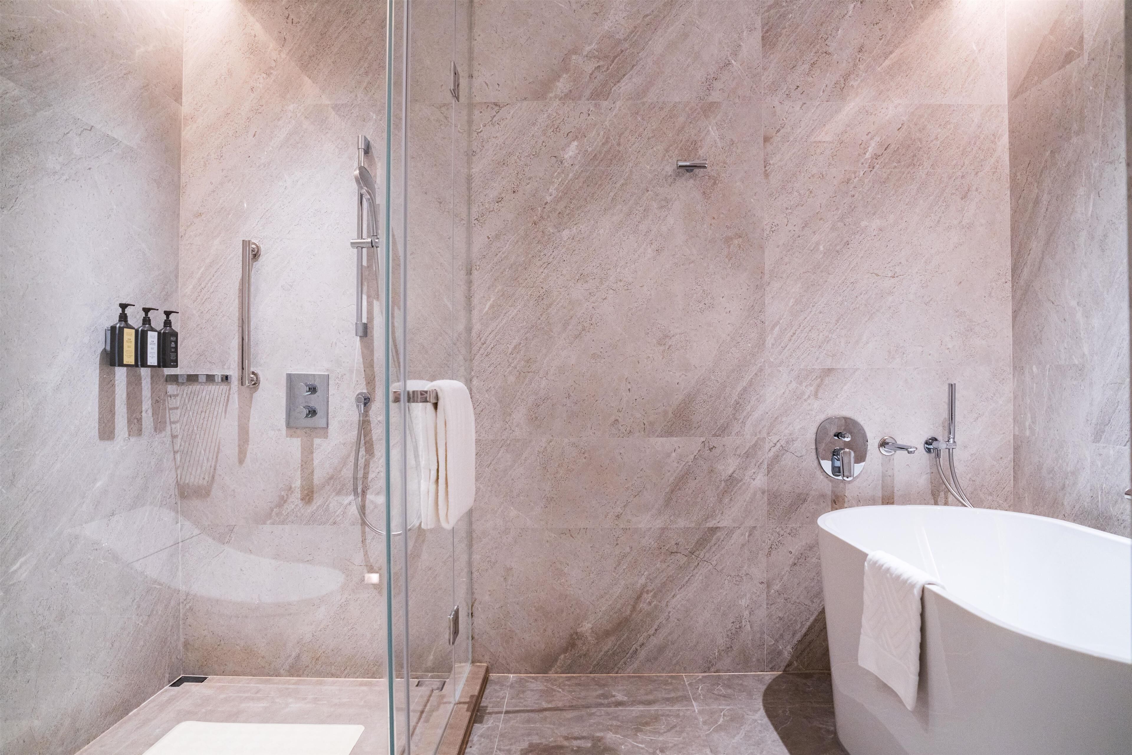 Une salle de bain moderne avec une douche à parois de verre, une baignoire sur pieds et des murs en marbre.