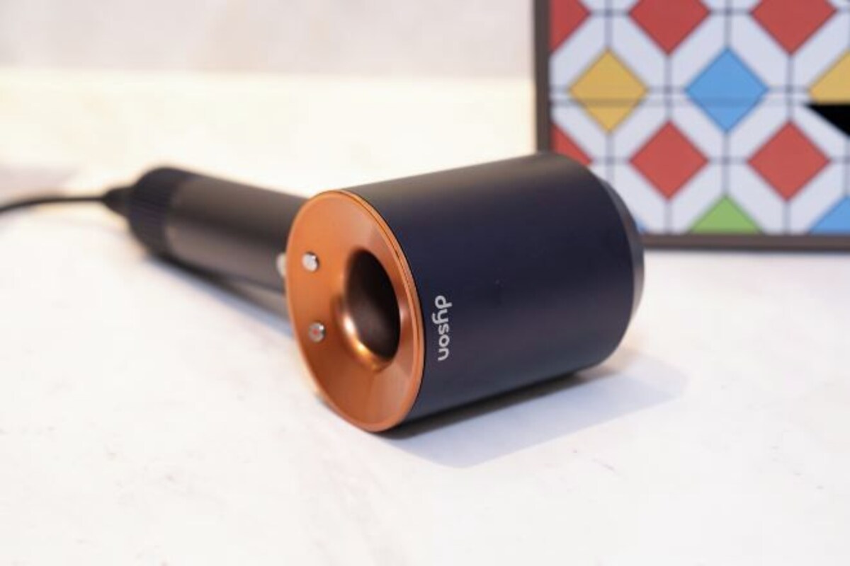 Un appareil cylindrique de couleur cuivrée, portant l’inscription « DJSFP », est posé sur une surface dont le fond est orné d’un motif géométrique.