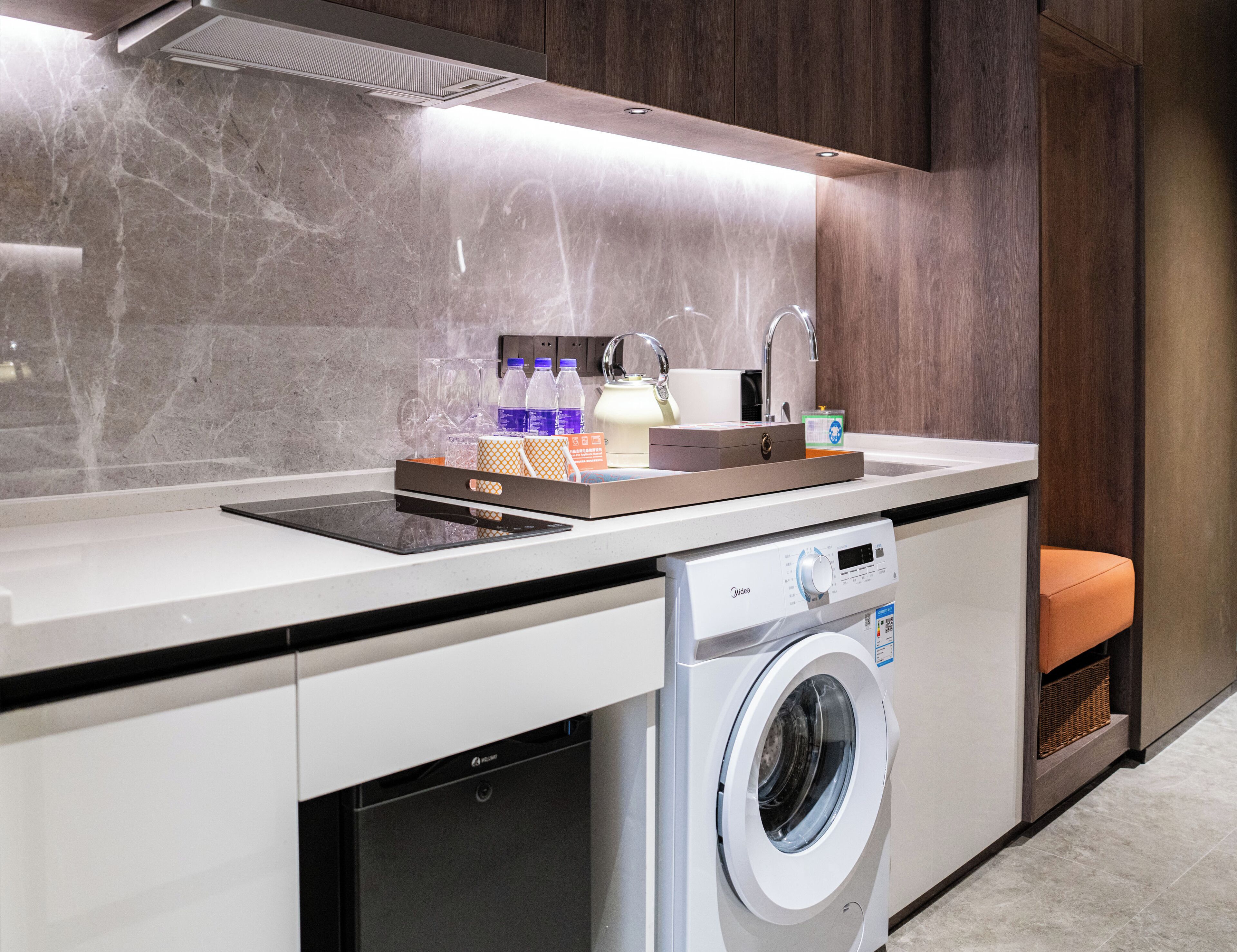A compact kitchen with a built-in washing machine, a countertop with a coffee machine, and a sink.
