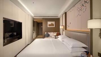 A hotel room with a large bed, a flat-screen TV, a bedside table with a lamp, and a wall-mounted TV.