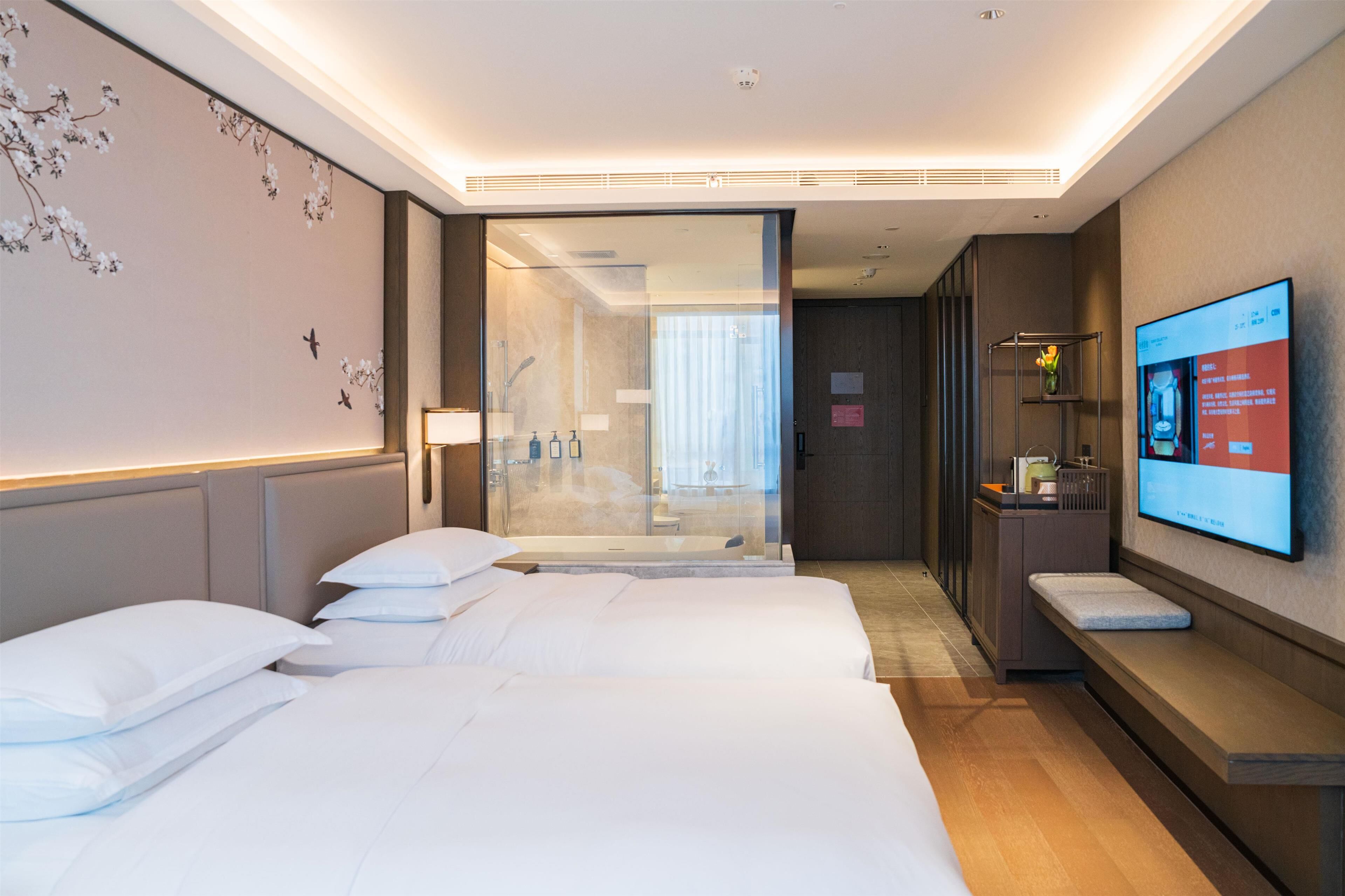 Habitación de hotel con dos camas, televisor, escritorio y zona de ducha.