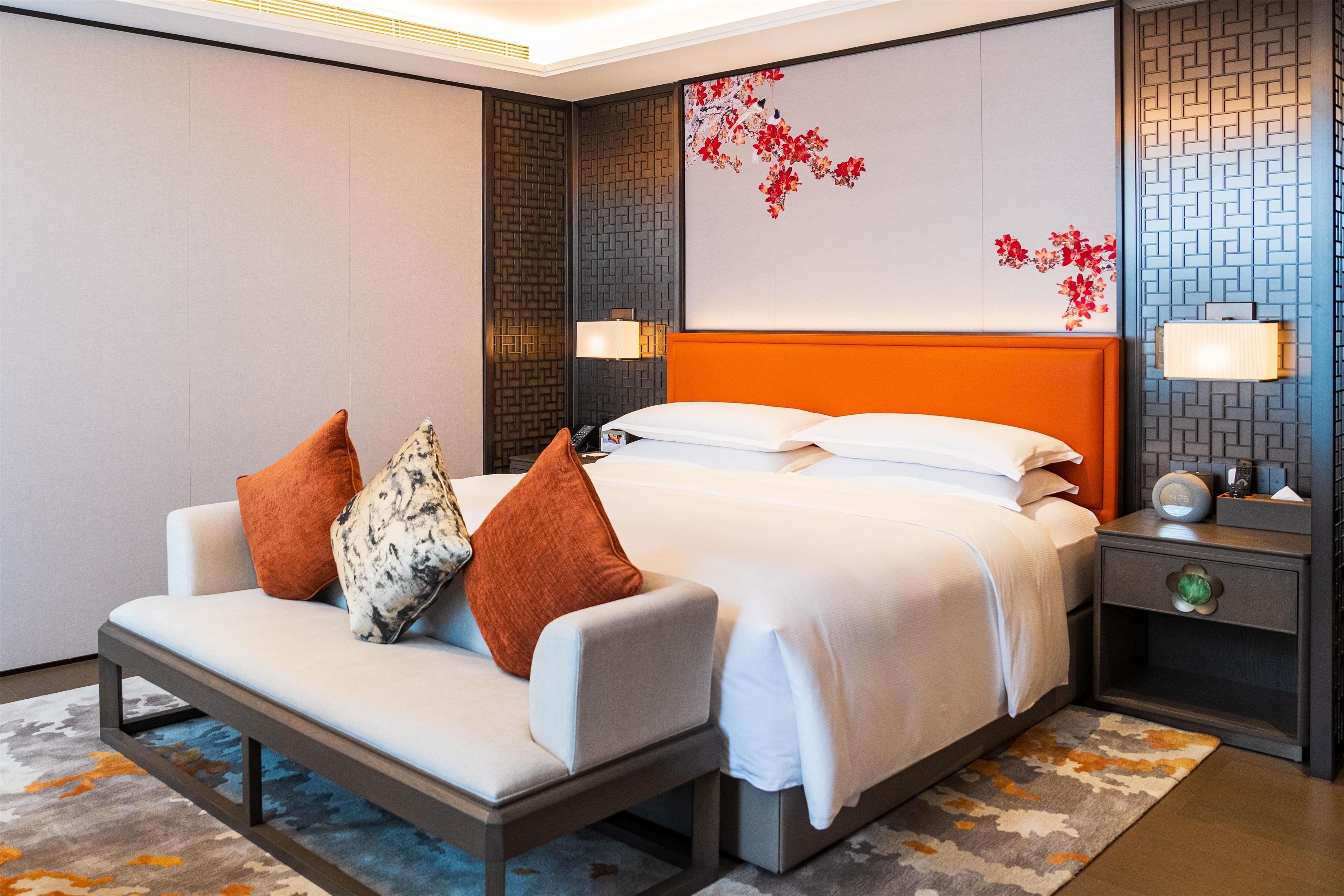 A modern hotel room with a bed, a sofa, a nightstand, and decorative wall art.