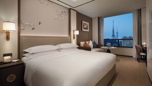 Habitación de hotel con una cama grande, lámparas de noche, una mesita con una silla y vistas a una torre.