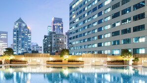 Un hotel moderno con una gran piscina, edificios altos al fondo y un espacio exterior bien iluminado.