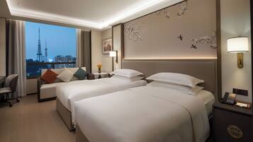A hotel room with two beds, a desk, a chair, a nightstand, and a view of a cityscape.