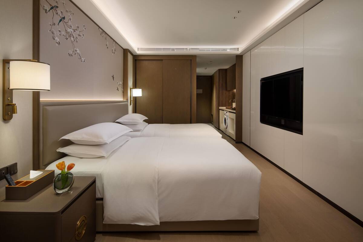 A hotel room with a large bed, a TV, a bedside table with a lamp, and a decorative wall.