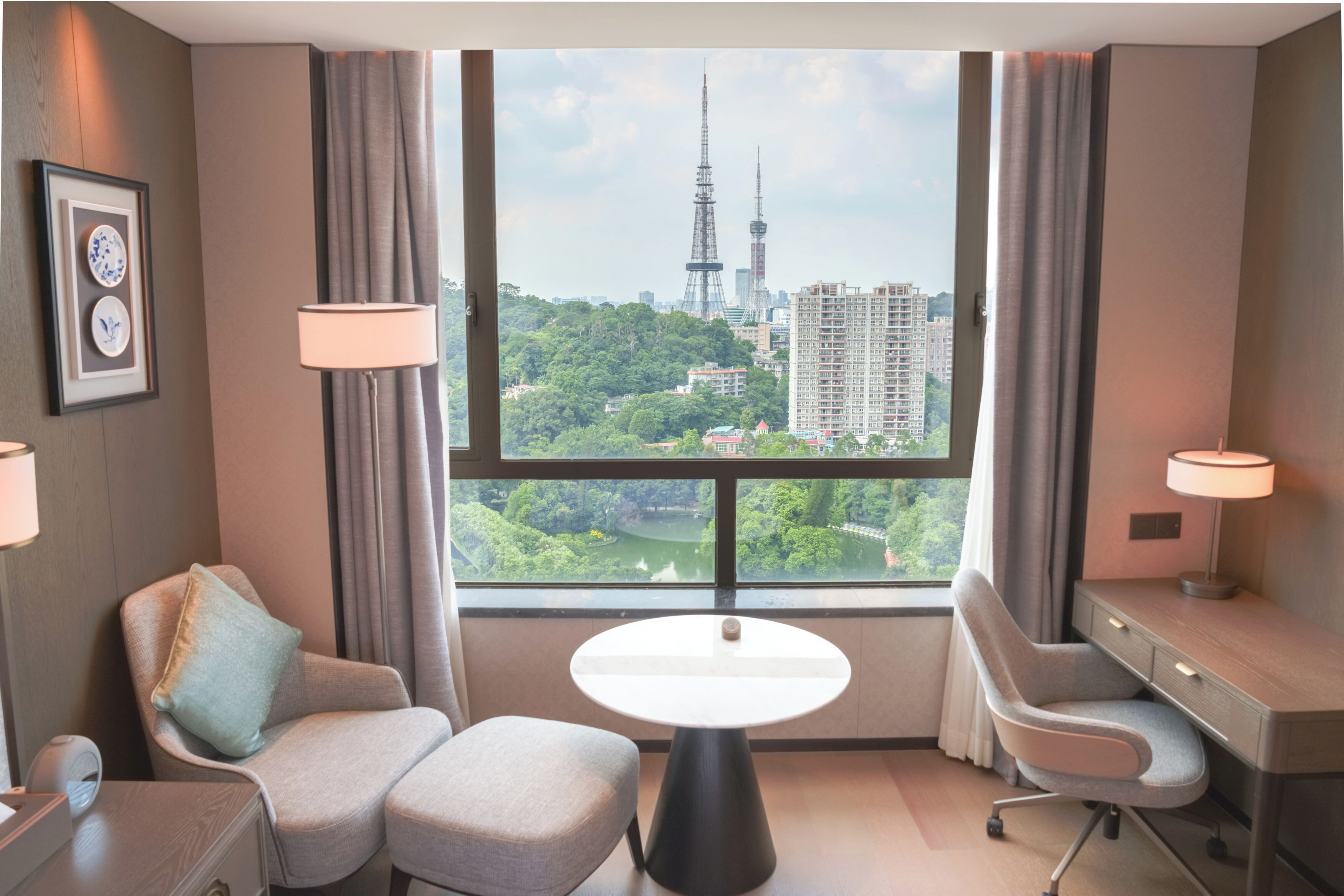 Una habitación de hotel con un ventanal grande, una mesa redonda, un sofá, un escritorio y una lámpara.