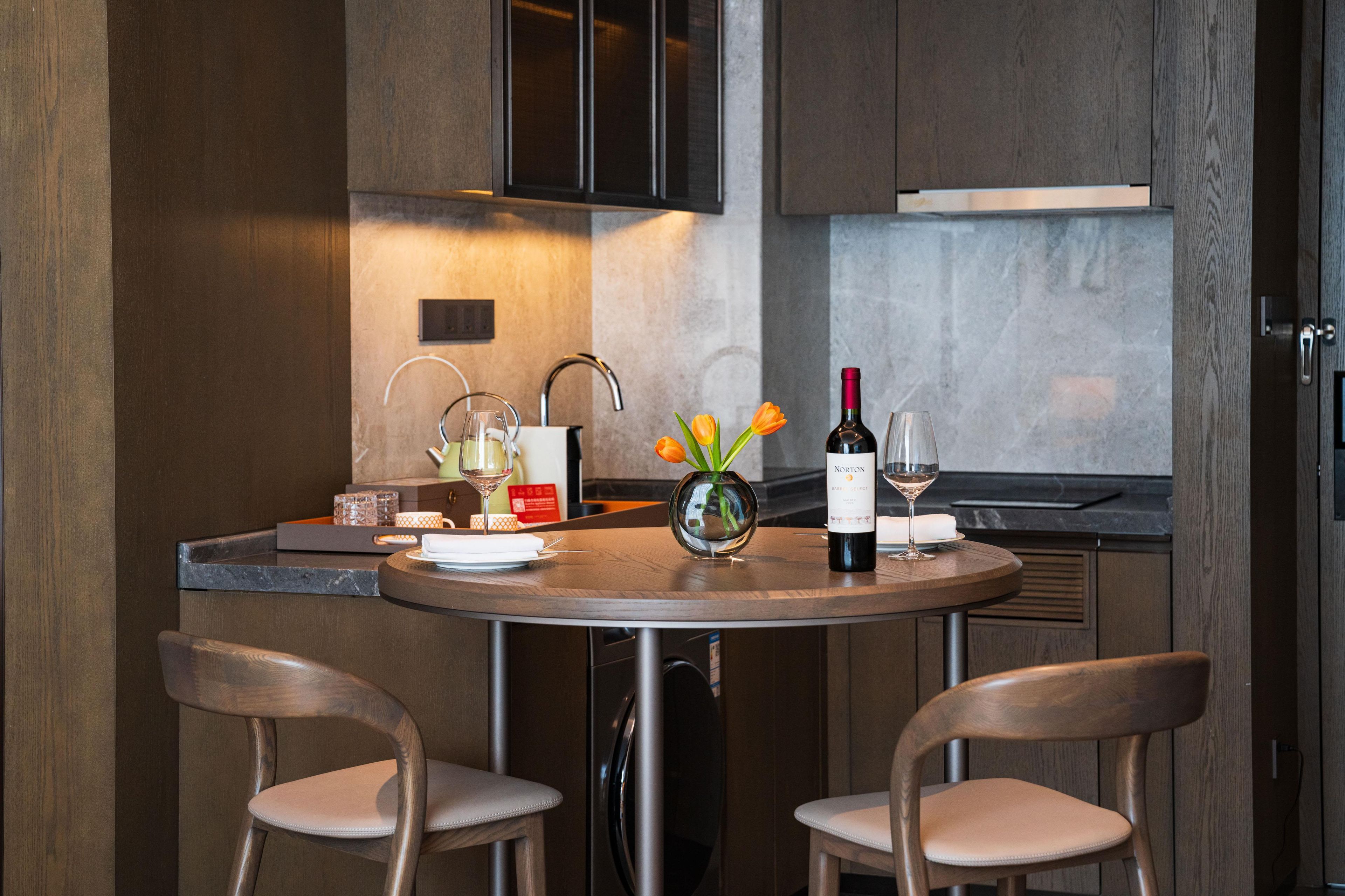 A modern kitchen with a round dining table, two chairs, a wine bottle, and a vase with flowers.