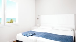 Quarto minimalista com uma cama grande, uma mesa de cabeceira e vista para o oceano pela janela.