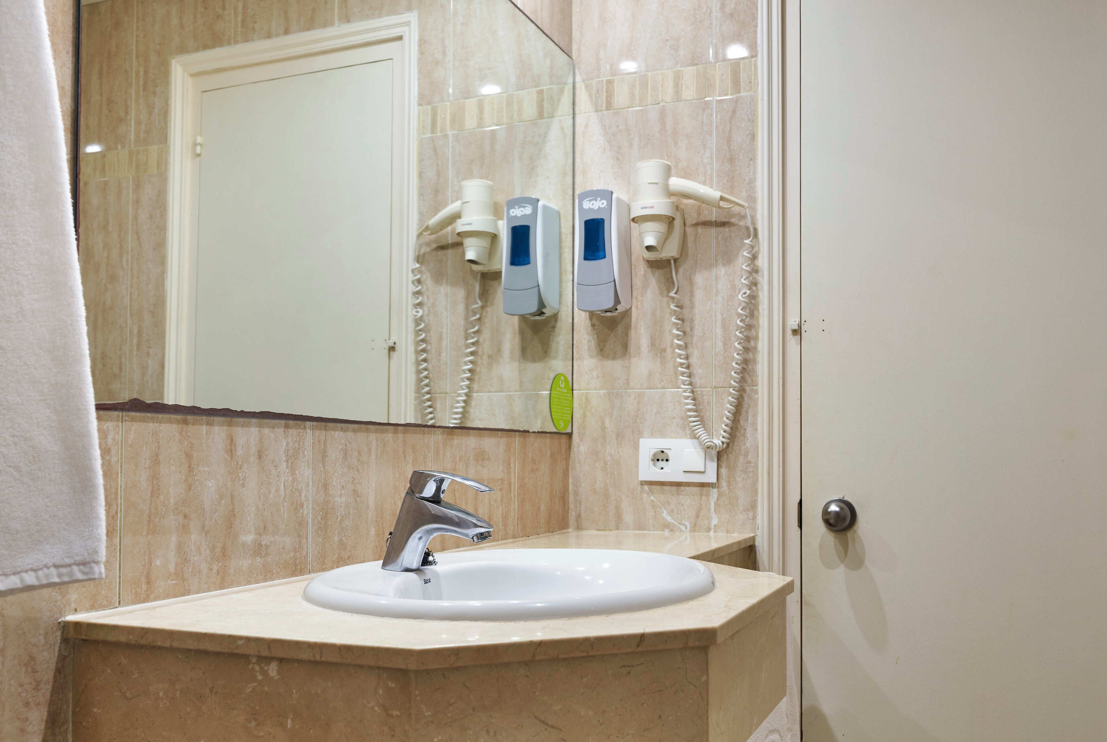 A bathroom with a sink, mirror, and hair dryers mounted on the wall.