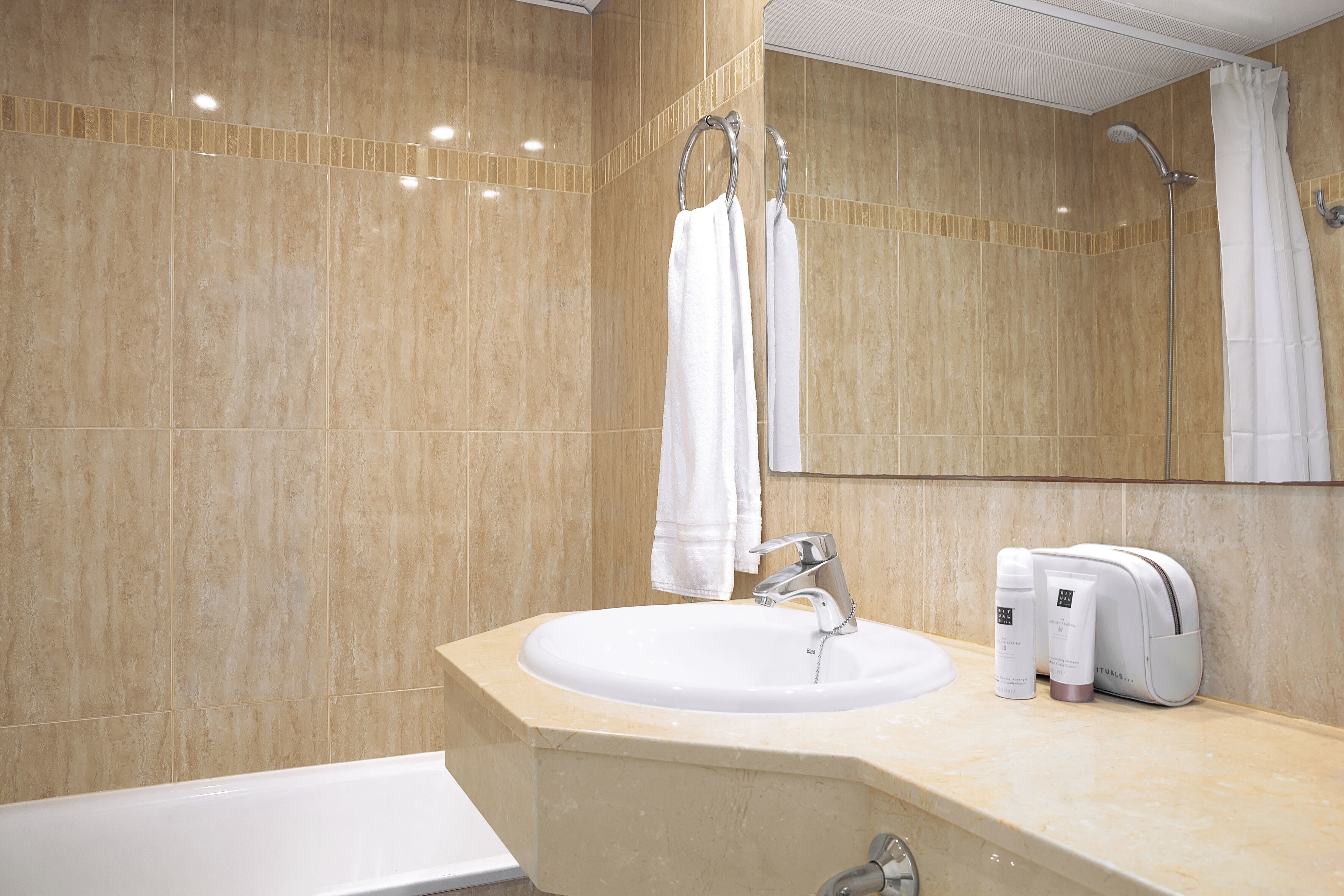 A bathroom with a sink, mirror, shower, and towel rack.