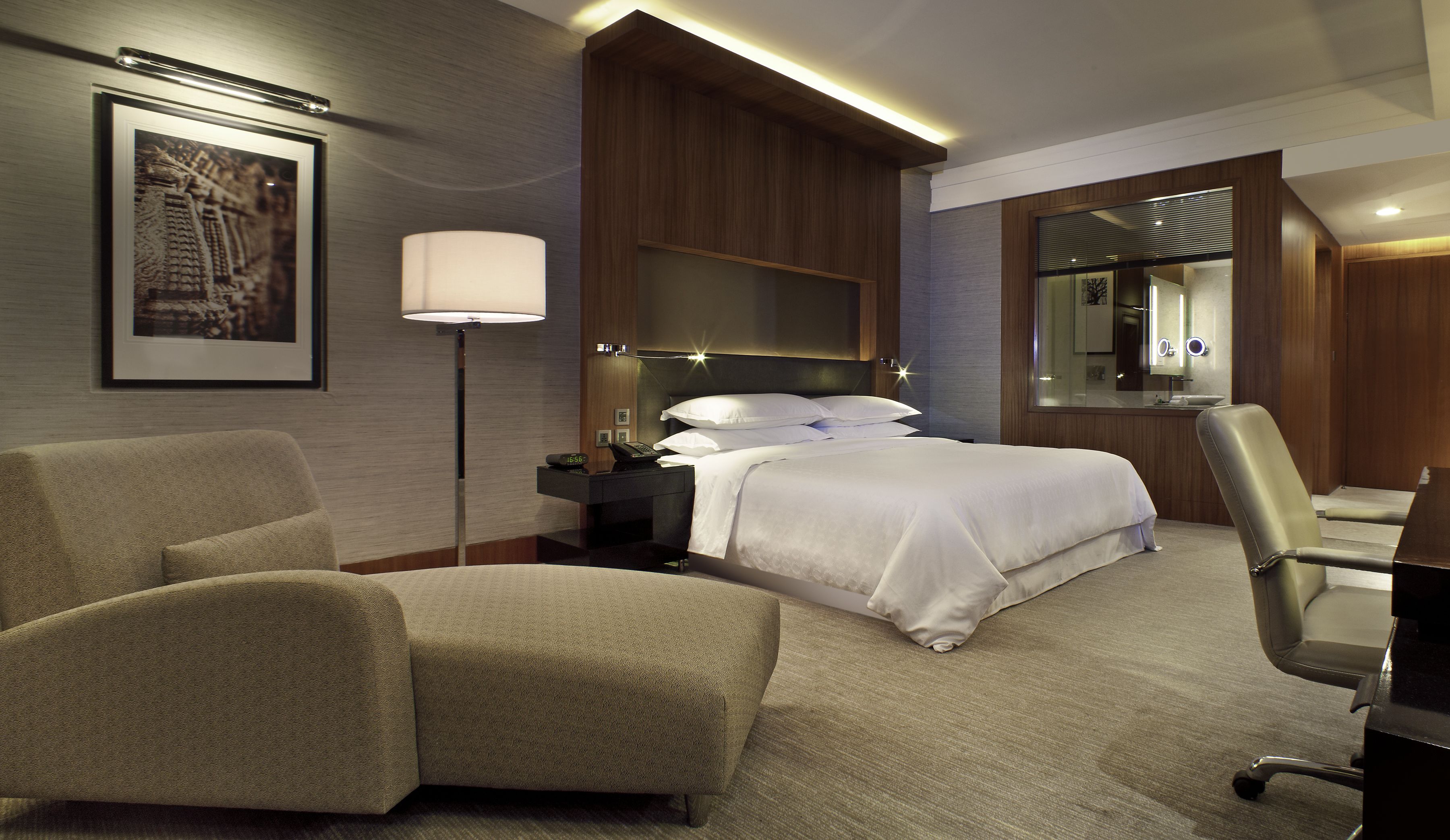 Habitación de hotel con cama, escritorio, silla, lámpara y un cuadro en la pared.