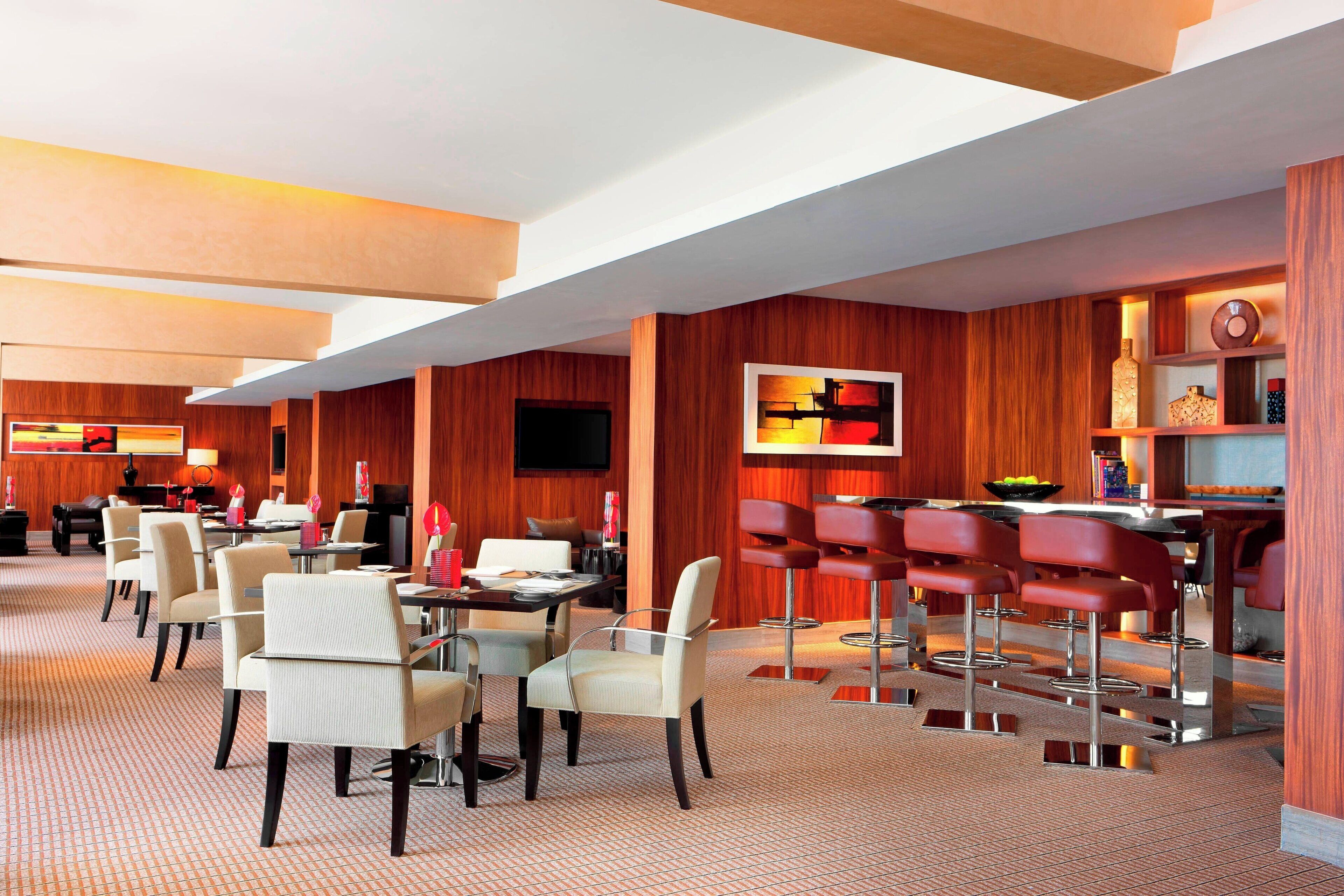 Un moderno vestíbulo de hotel con zona de bar, asientos y una pantalla de televisión.