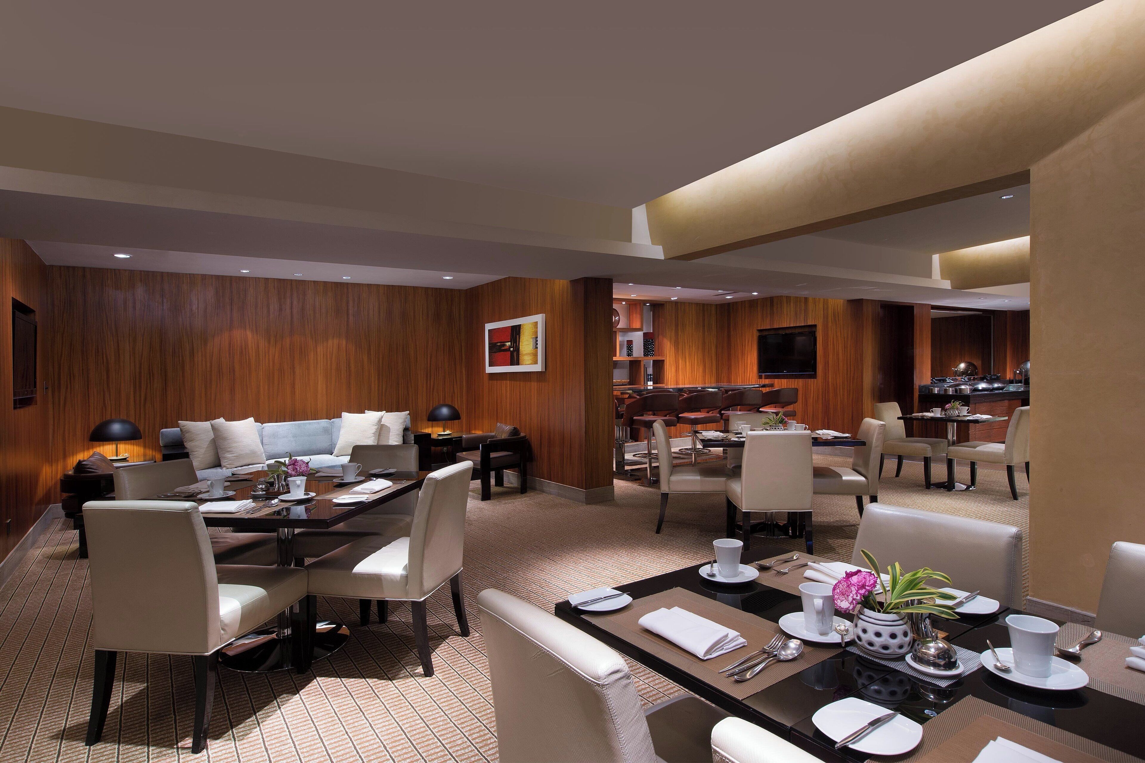 Un comedor de hotel moderno con paneles de madera, varias mesas y asientos cómodos.