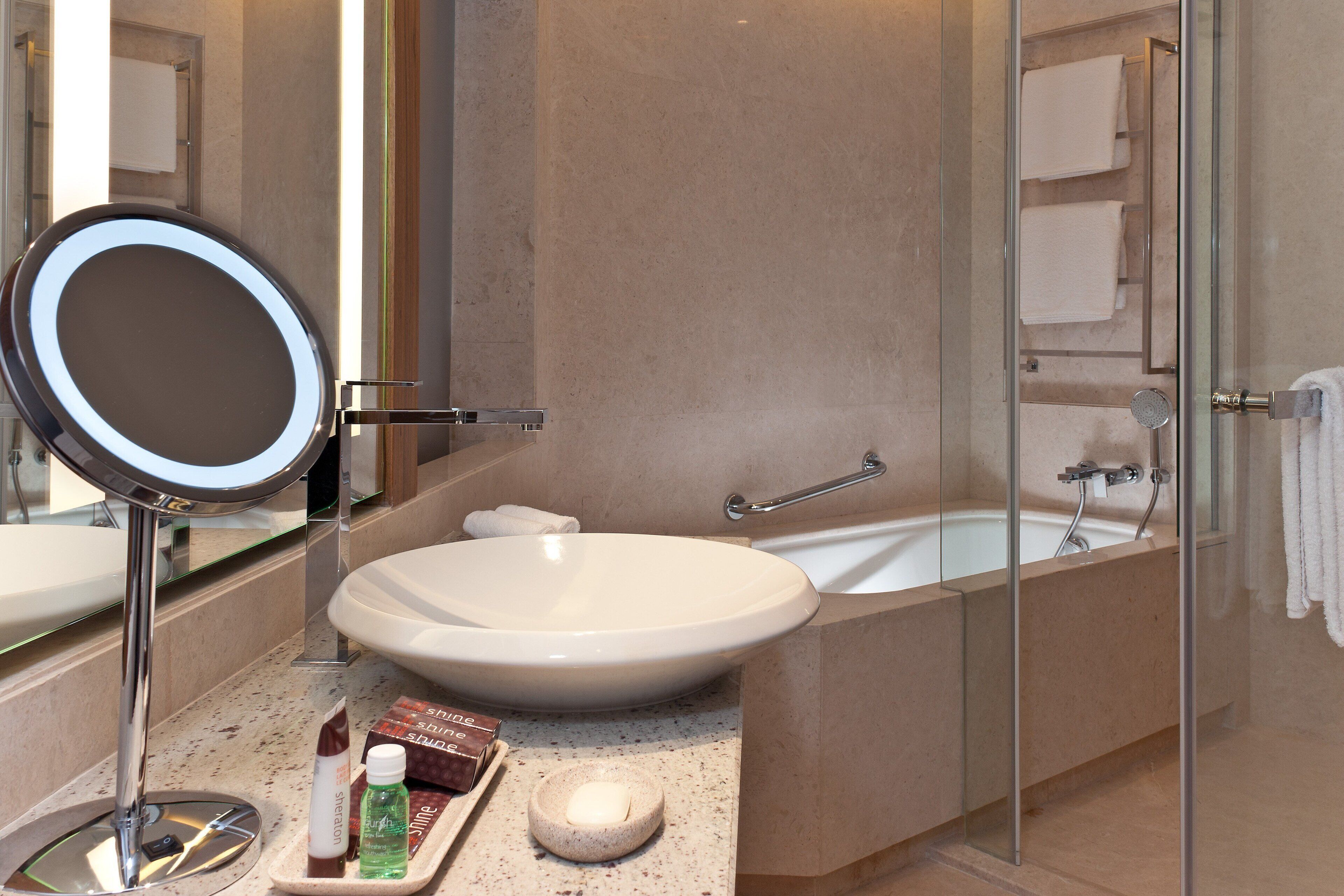 A bathroom with a large oval sink, a round mirror, a bathtub, and a glass-enclosed shower.