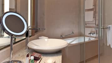A bathroom with a large oval sink, a round mirror, a bathtub, and a glass-enclosed shower.