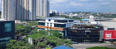 A high-rise building with a rooftop pool and lounge area, surrounded by greenery and other buildings.