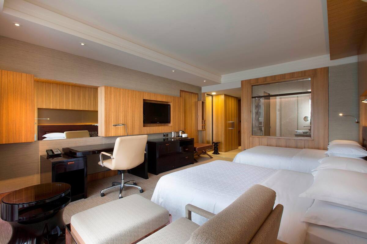 Habitación de hotel con cama, escritorio, silla, televisor y espejo.