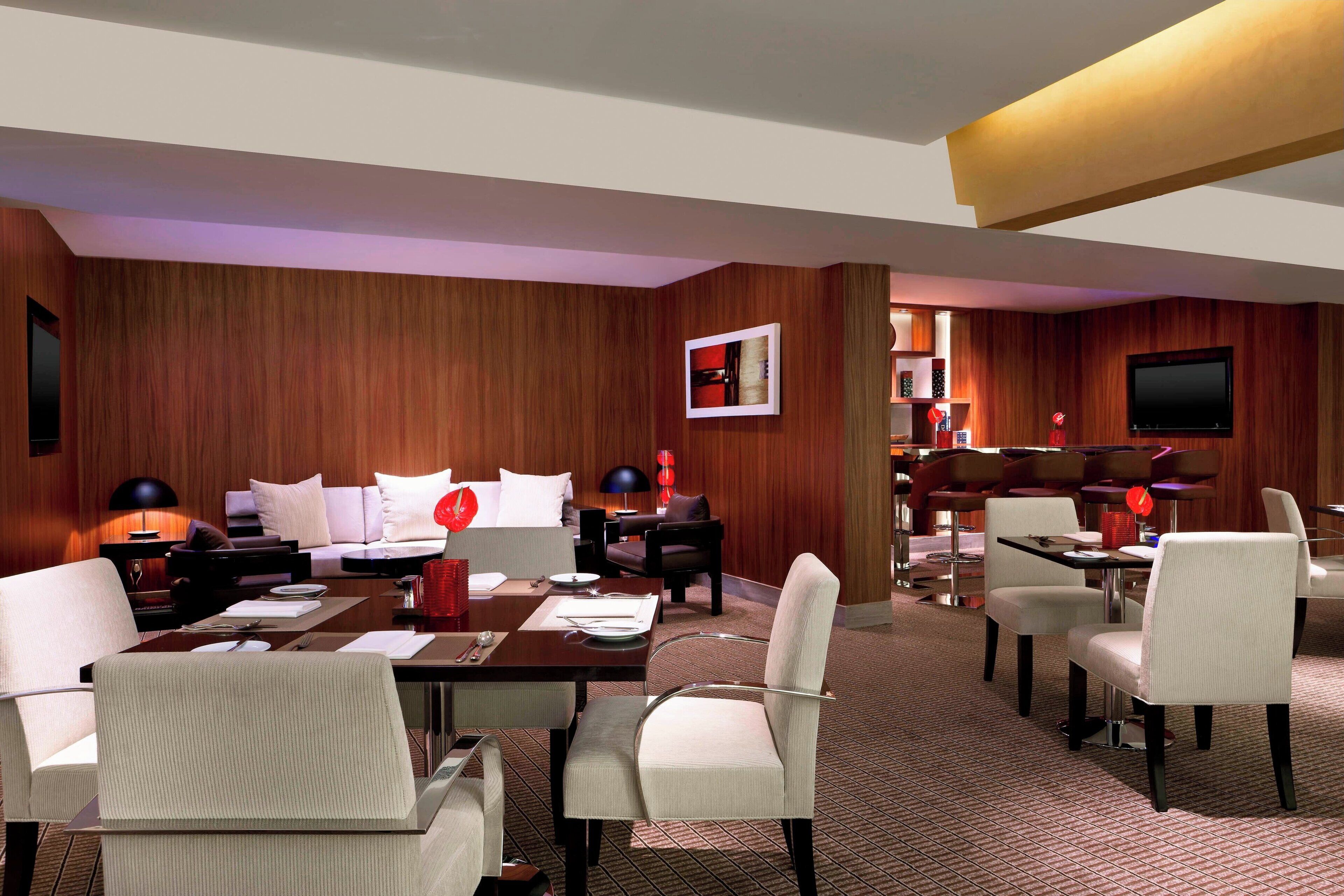 Habitación de hotel con pared de madera, televisor de pantalla plana, zona de comedor con mesa y sillas, y un sofá.