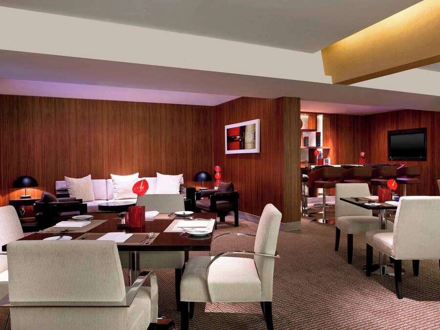Habitación de hotel con pared de madera, televisor de pantalla plana, zona de comedor con mesa y sillas, y un sofá.