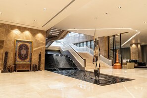 Een moderne lobby met een marmeren vloer, een groot decoratief tapijt, een trap en een fontein.