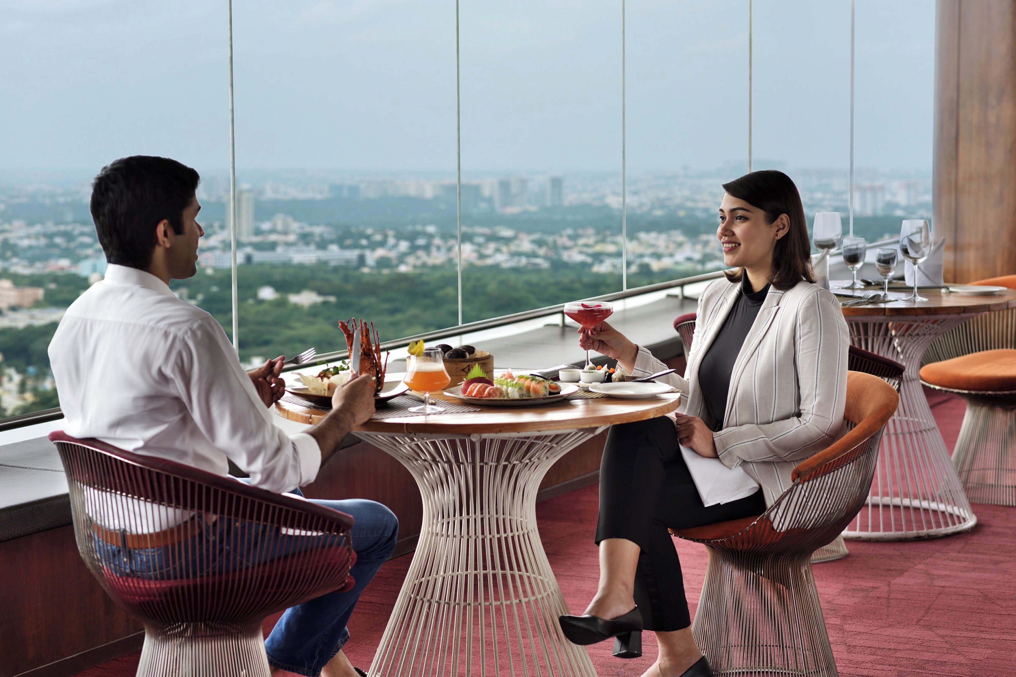 Un restaurante en un edificio alto con vistas panorámicas de la ciudad, mesas redondas y sillas de mimbre.