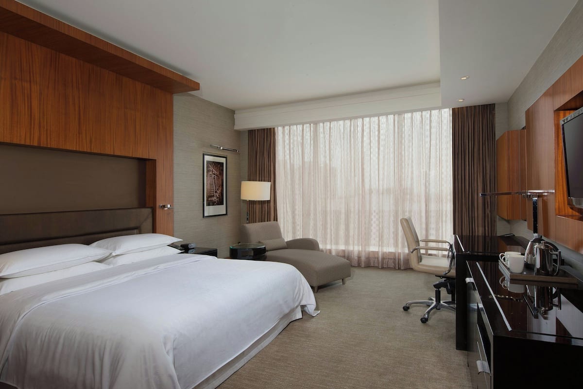 Una habitación de hotel con dos camas, un escritorio con silla, un televisor y un ventanal con cortinas.