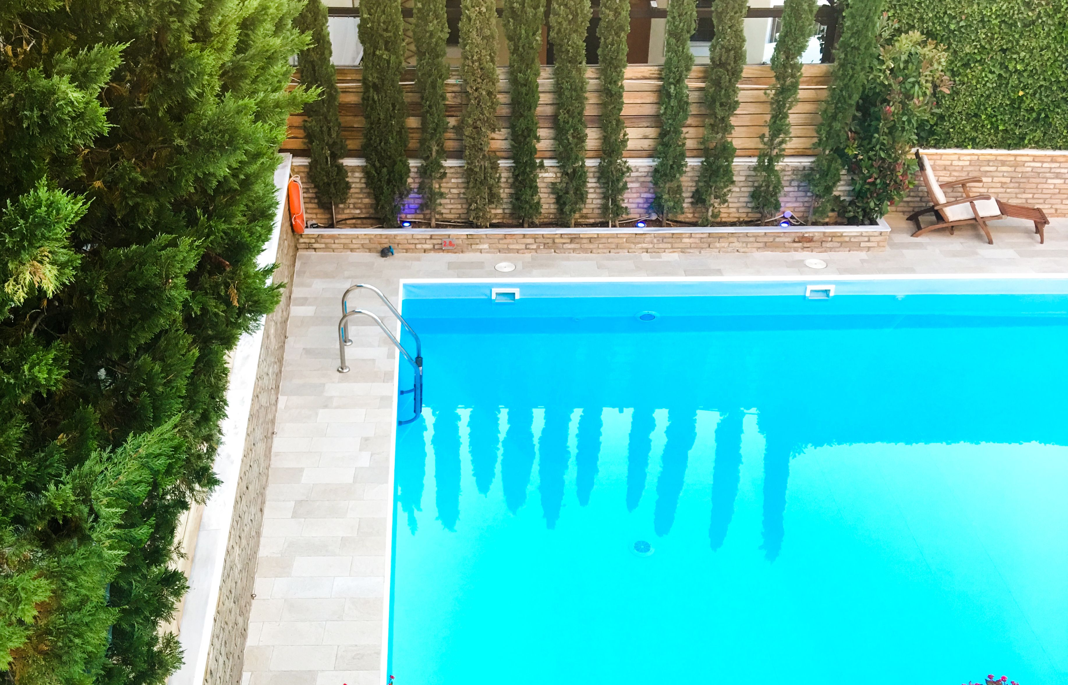 Una piscina con una scala in metallo, circondata da un muro in mattoni e vegetazione.