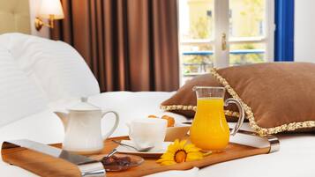 A neatly made breakfast tray with a pitcher of orange juice, a cup of coffee, and pastries on a bed with white bedding and a brown pillow.
