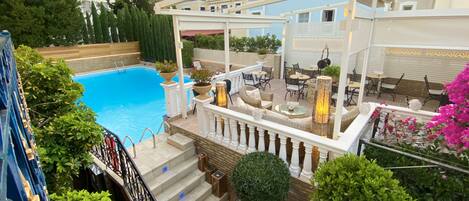 Un espace aménagé au bord de la piscine, doté d’une pergola, de sièges d’extérieur et d’un escalier menant à une terrasse.