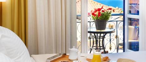 A hotel room with a balcony, a breakfast tray with croissants, a coffee pot, a pitcher of orange juice, and a sun-shaped napkin.