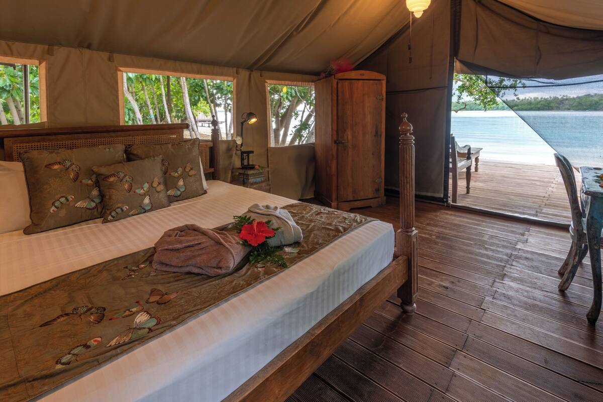A tented room with a bed, wooden flooring, and a view of a lake.